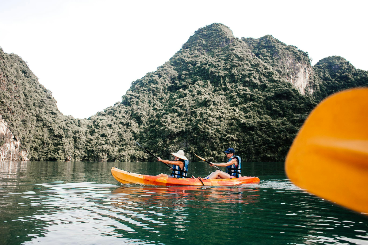 Tourist kayaking through calm green waters surrounded by rocky islets in Ha Long Bay