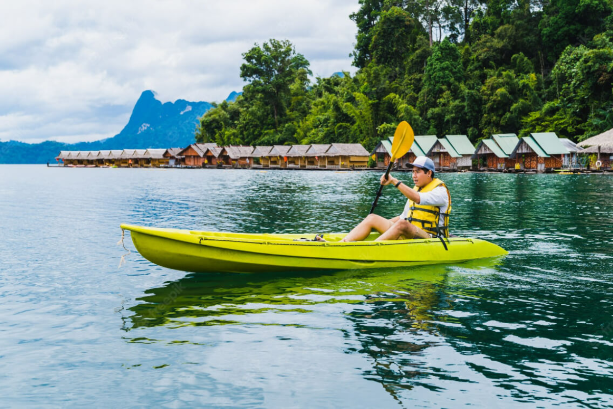 Traveler kayaking on Cheow Lan Lake with limestone cliffs and jungle in background