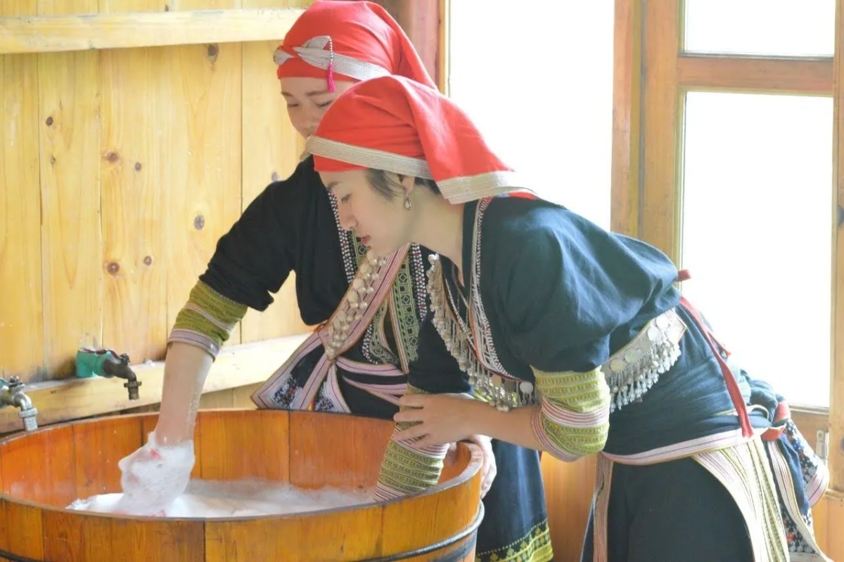 Red Dao women preparing a traditional herbal bath in a wooden tub in Sapa