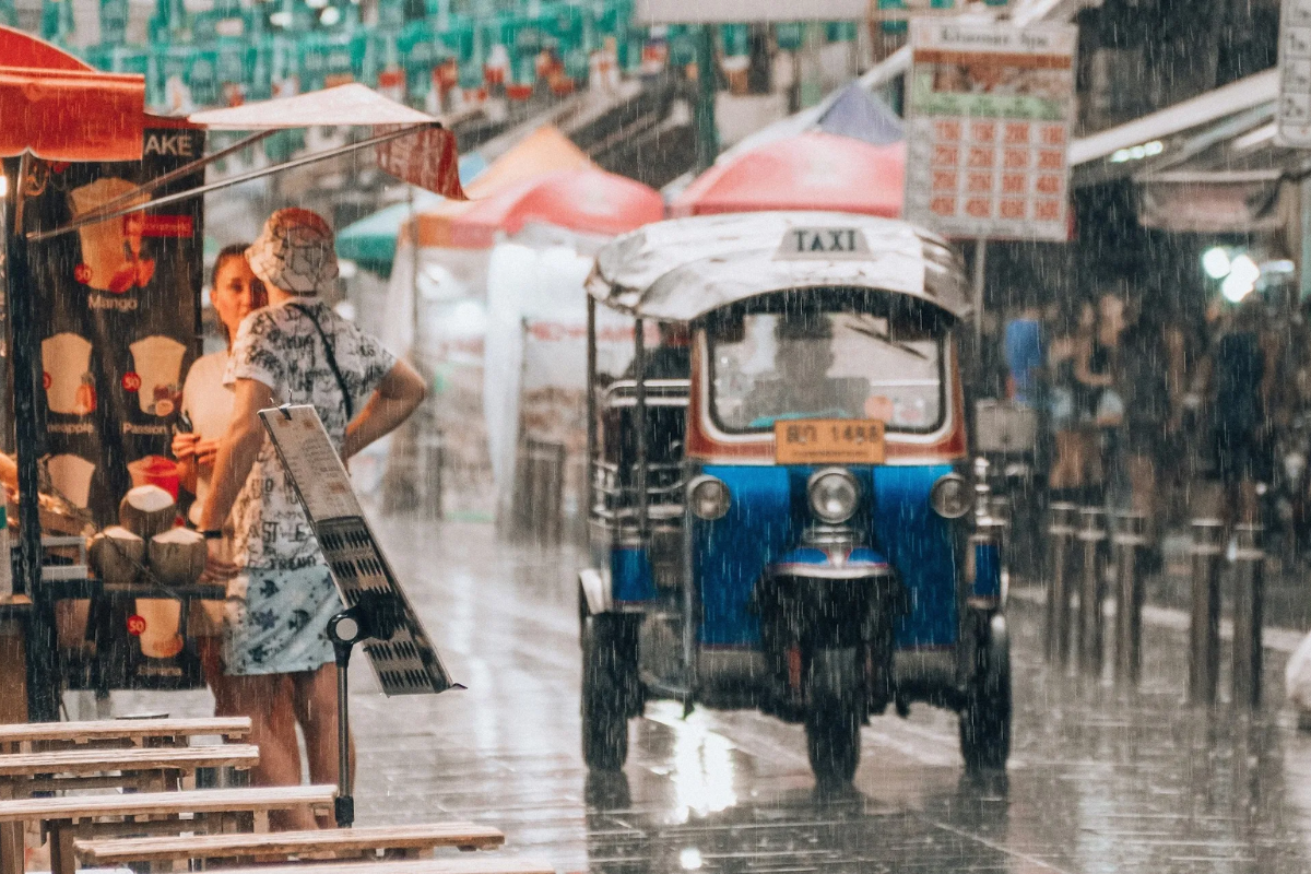 Rain-soaked street in Bangkok during August with people using umbrellas
