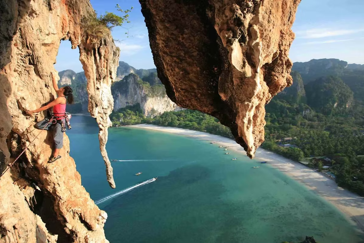 Climber scaling limestone cliffs with scenic ocean view at Railay Beach in southern Thailand