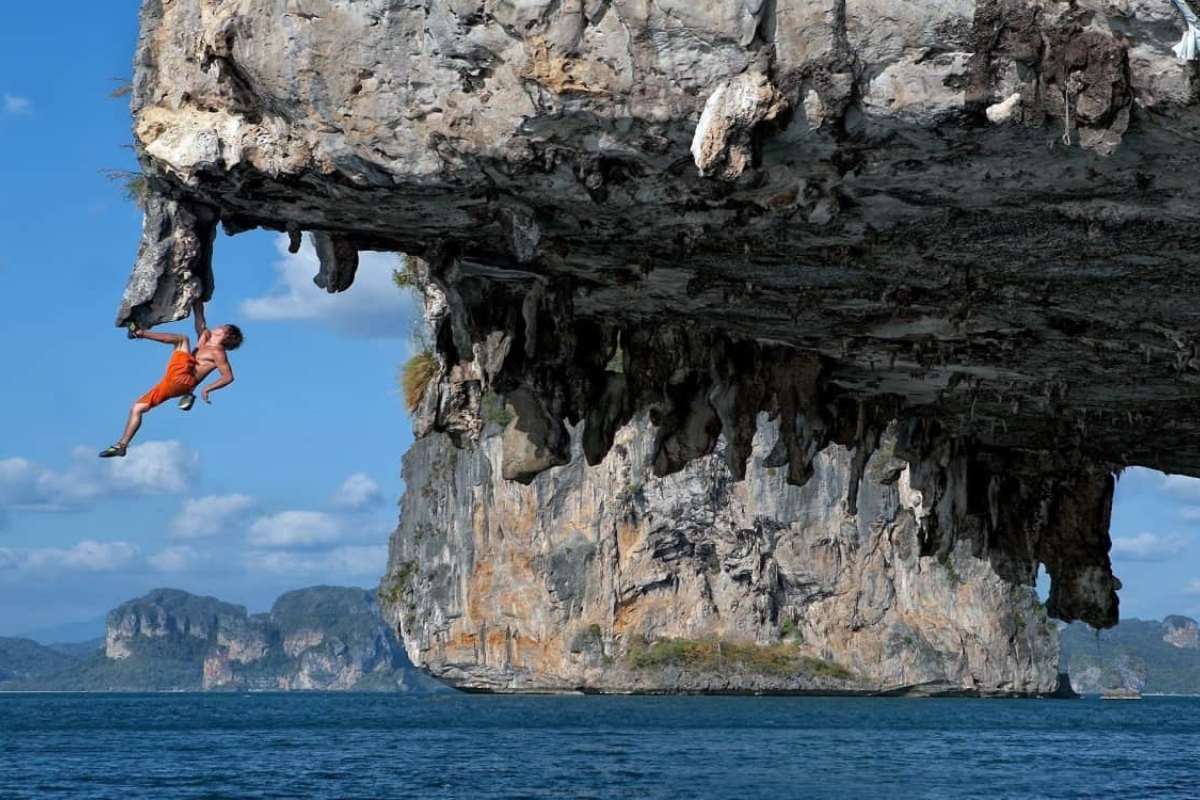 Climber ascending a limestone cliff in Ha Long Bay with the sea below