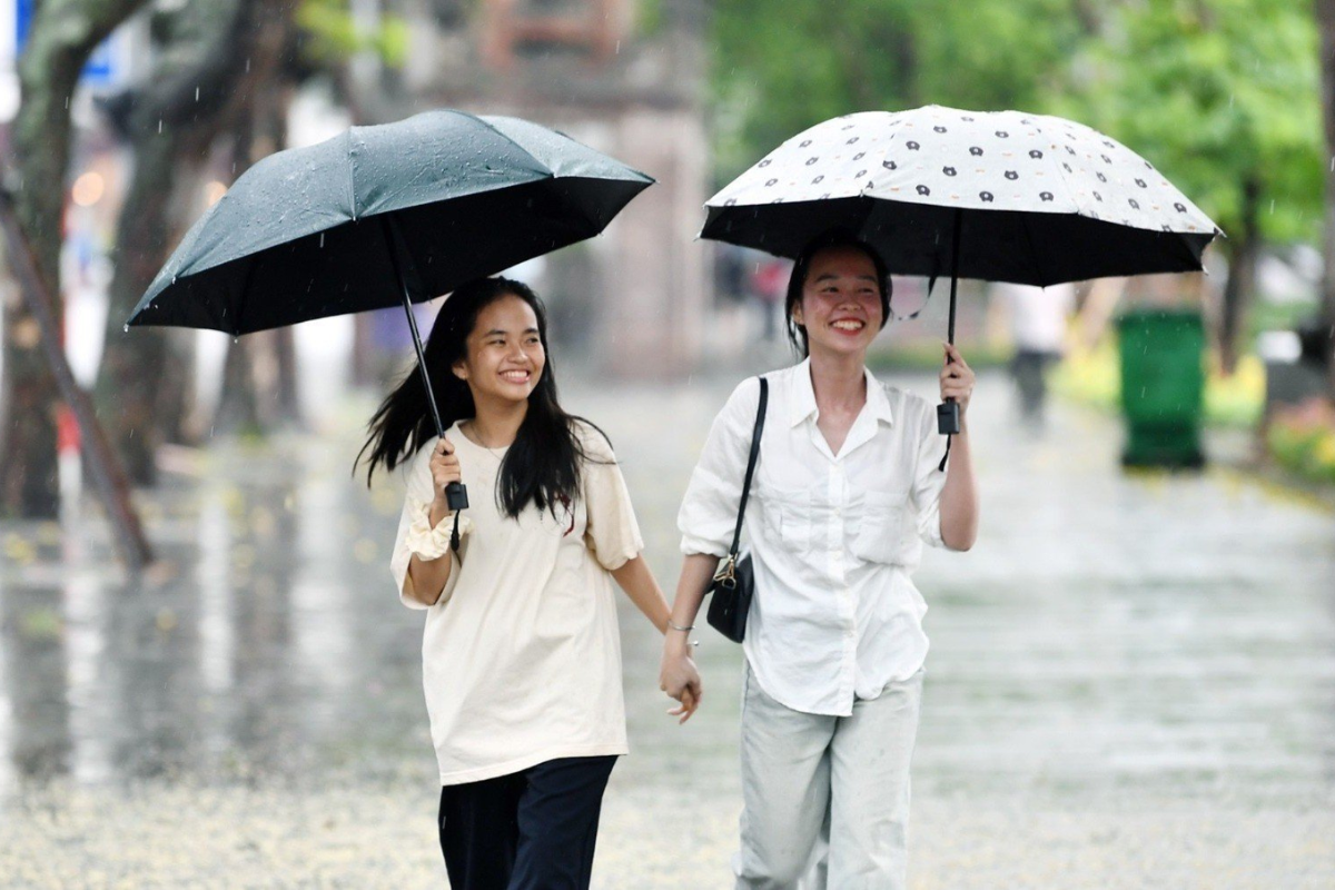 Locals navigating Hanoi's streets under umbrellas during June rain