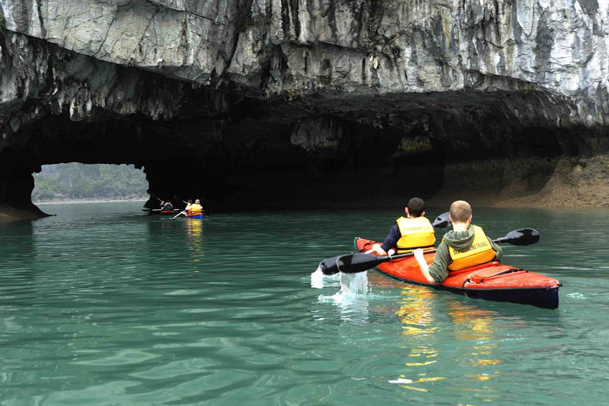 Tourists kayaking around limestone caves in Ha Long Bay under a sunny August sky