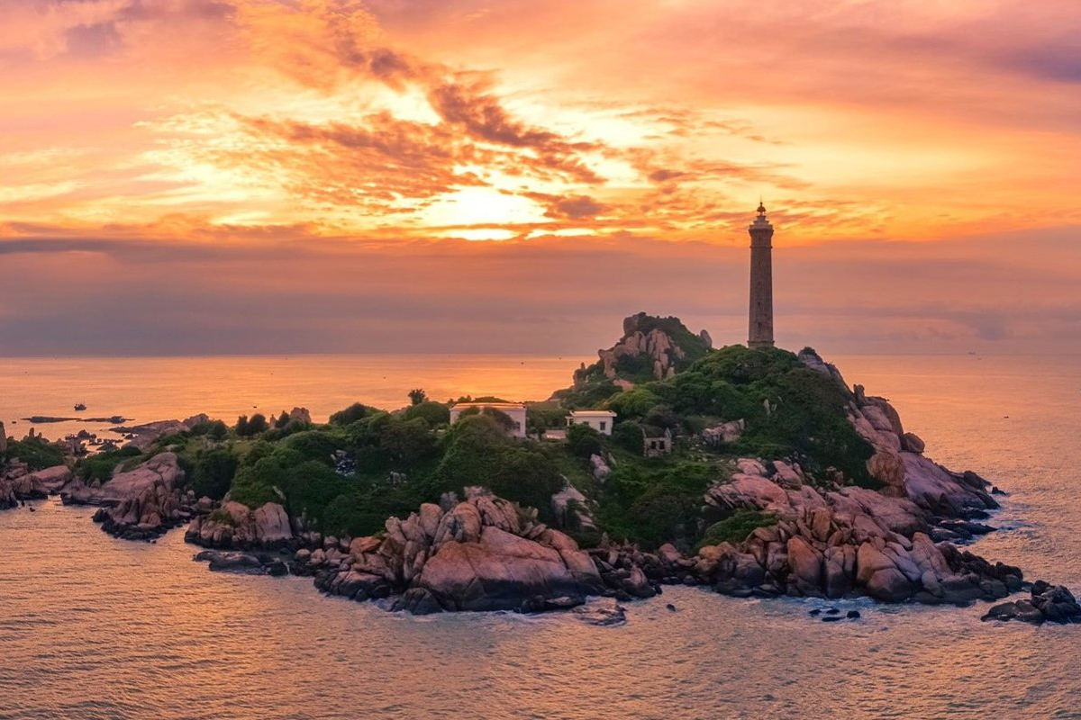 Golden sunset over Ke Ga Lighthouse viewed from the shore with waves gently crashing