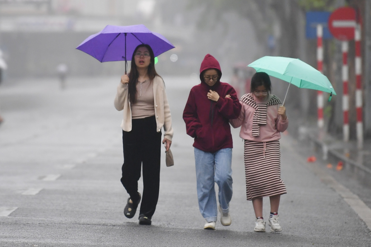 Light rain falling on a Hanoi street with people using umbrellas and scooters parked nearby