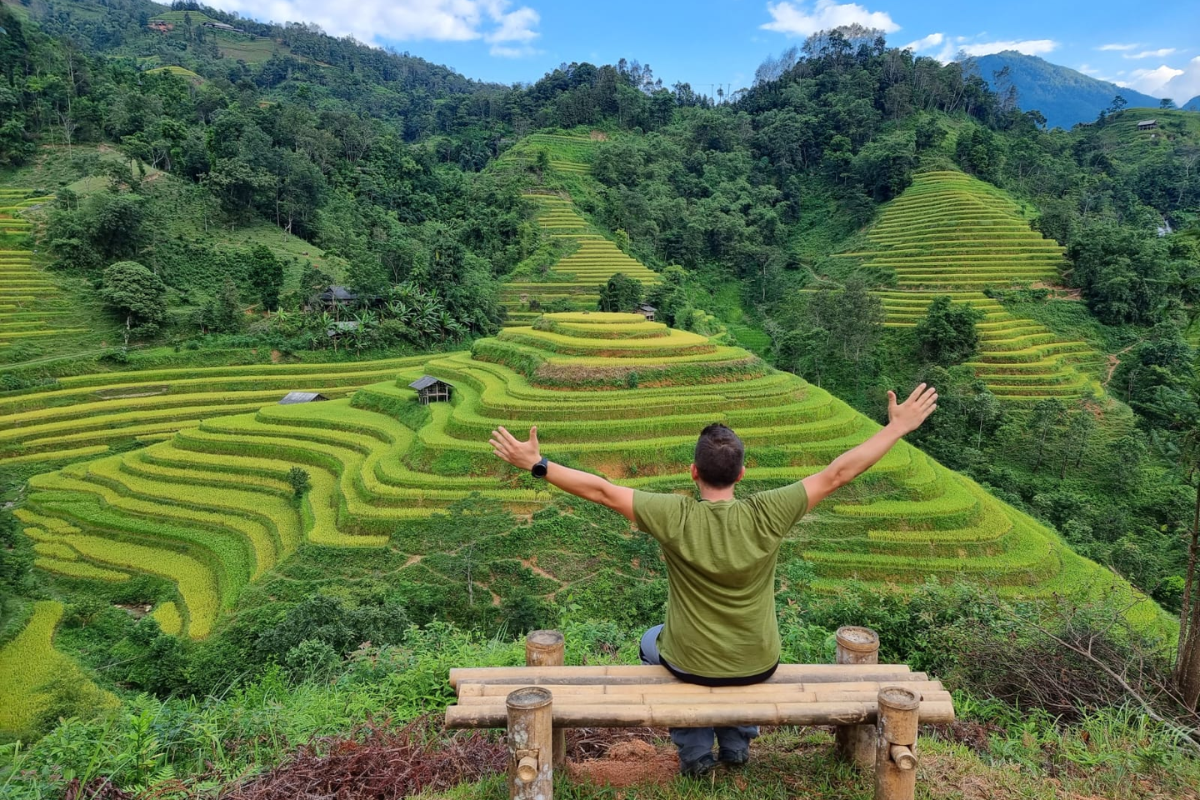 Trekker walking along a narrow trail above rice terraces in the Hoang Su Phi mountains.