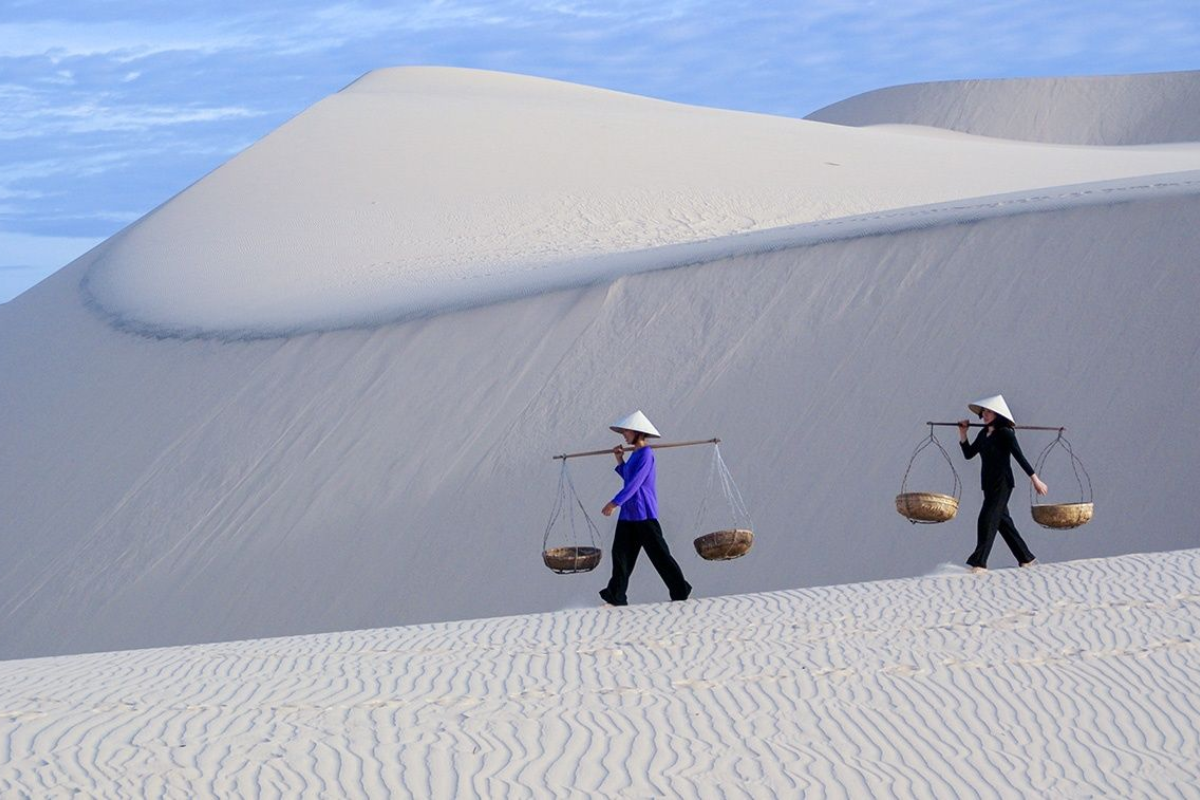 A panoramic view of the White Sand Dunes Mui Ne with white sand hills under a bright blue sky, attracting many tourists